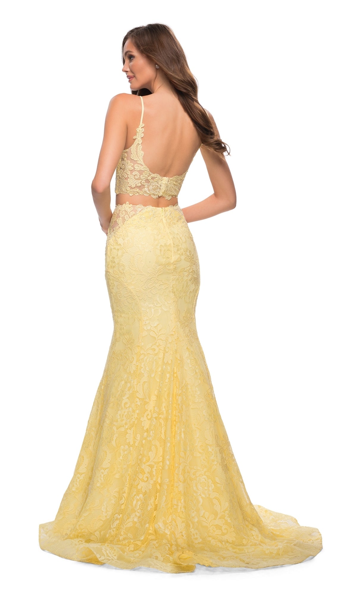 A woman faces away from the camera in the La Femme 29970, a two-piece yellow lace mermaid prom dress with thin straps and an open back.
